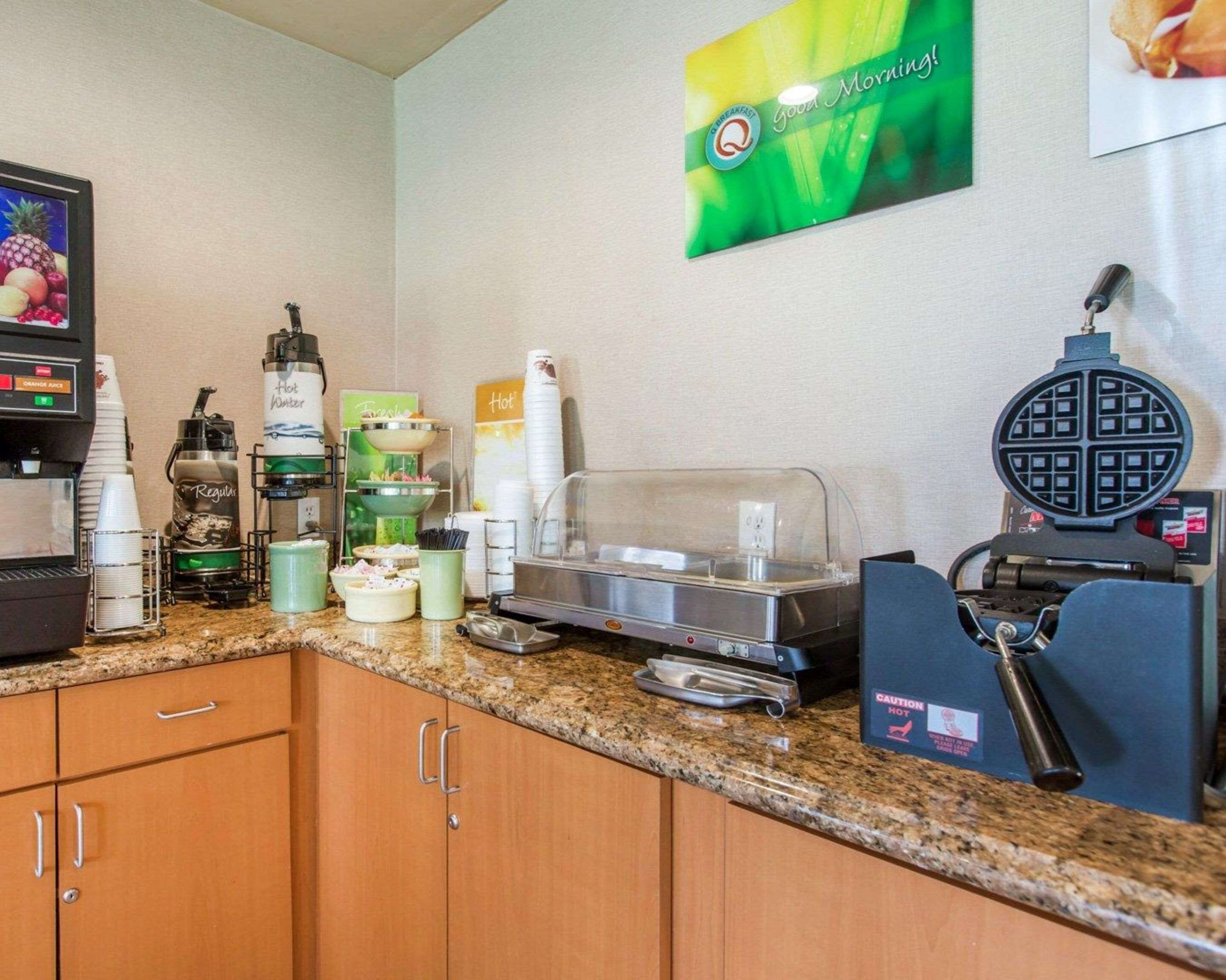 A hotel breakfast area with a coffee machine, hot water dispenser, and waffle maker.