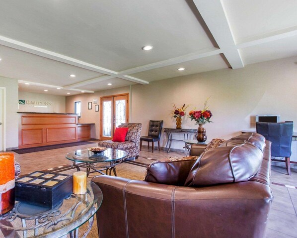 A spacious lobby with a reception desk, leather seating, a glass coffee table, and a vase with flowers.