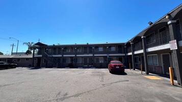 A multi-story motel with a parking lot, a staircase leading to the entrance, and a red car parked in the lot.