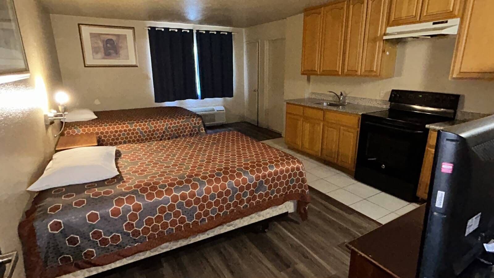 Quarto de hotel compacto com duas camas, uma kitchenette e um banheiro pequeno.