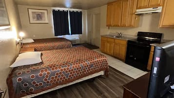 Quarto de hotel compacto com duas camas, uma kitchenette e um banheiro pequeno.