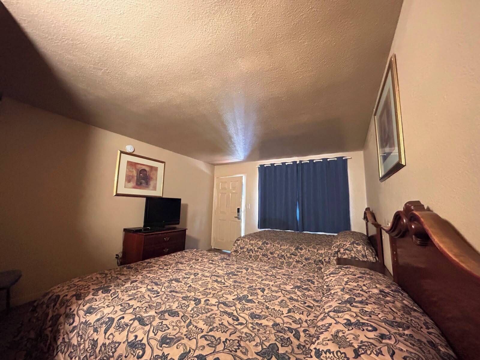 A hotel room with a bed, a television on a dresser, a door, and a window with curtains.
