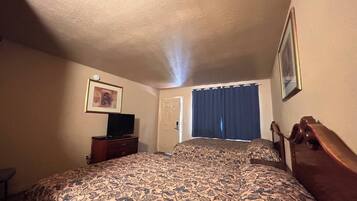 A hotel room with a bed, a television on a dresser, a door, and a window with curtains.