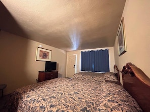 Een hotelkamer met een bed, een televisie op een dressoir, een deur en een raam met gordijnen.
