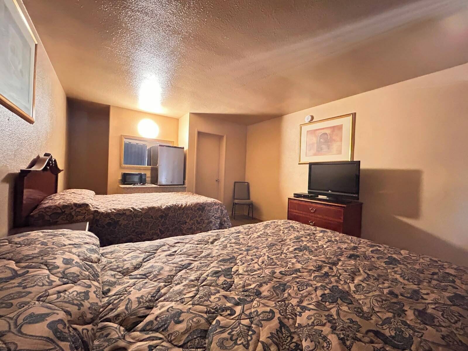 Een hotelkamer met twee bedden, een televisie, een dressoir en een spiegel.
