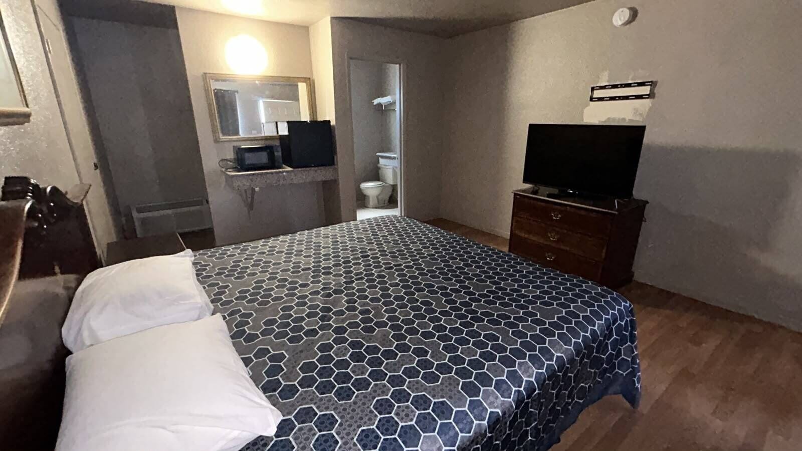 A hotel room with a bed, a television, a mirror, and a bathroom visible through an open door.