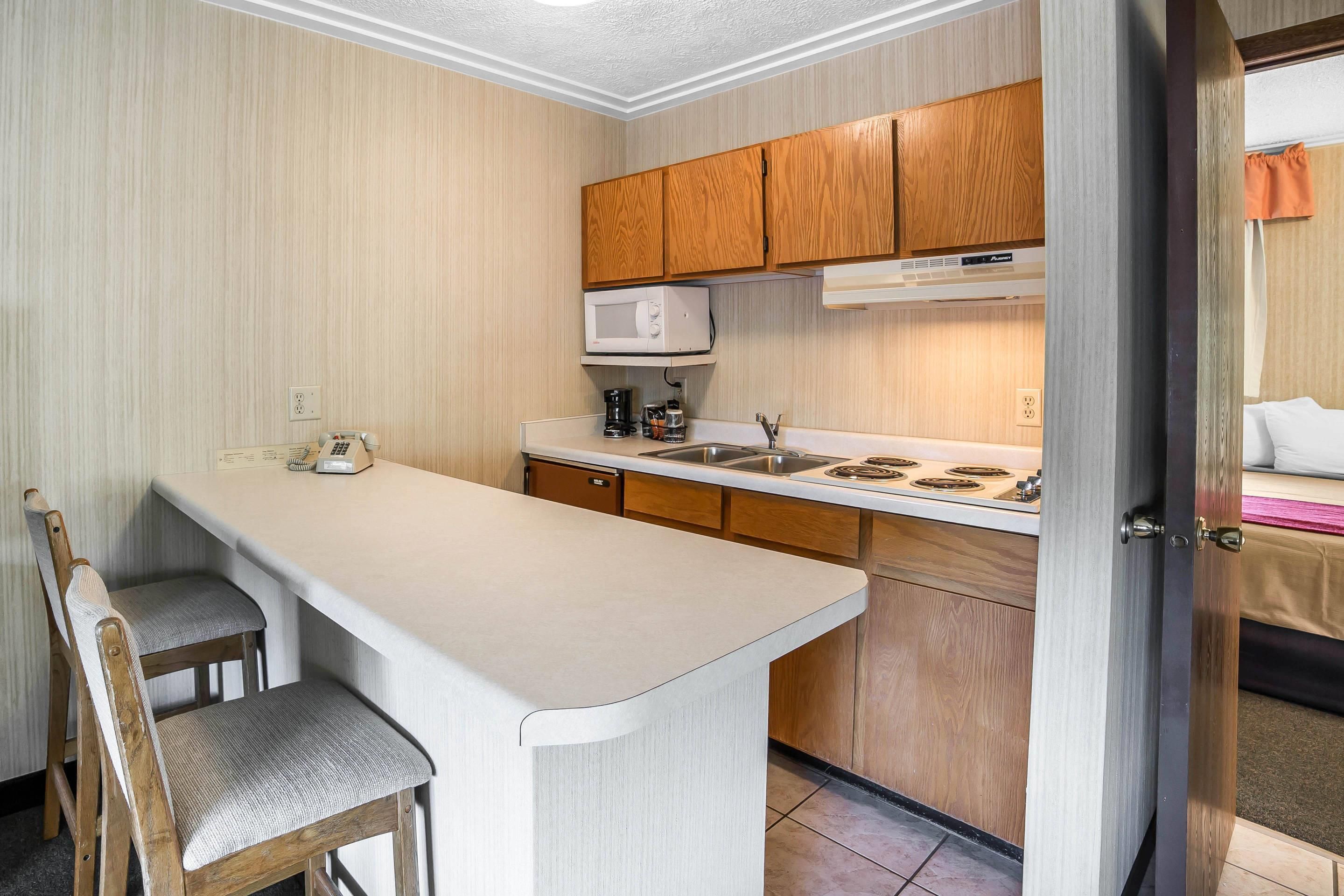 A compact kitchen with wooden cabinets, a microwave, a sink, and a small bar area with chairs.