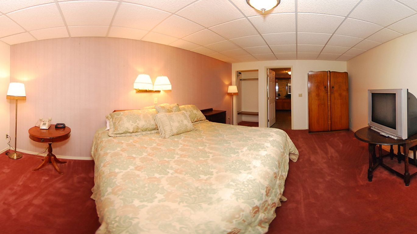 A hotel room with a large bed, a television, a desk, and a lamp.