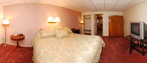 A hotel room with a large bed, a television, a desk, and a lamp.