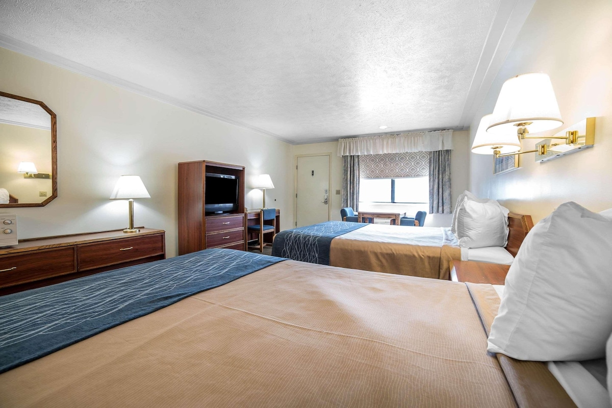 A hotel room with two beds, a desk, a dresser, a TV, and a window with curtains.
