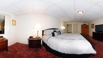 A bedroom with a large bed, a nightstand with a lamp, a dresser, a television, and a wardrobe.