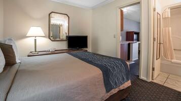 Una habitación de hotel con una cama, televisión, lámpara, espejo y puerta al baño.