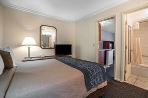 A hotel room with a bed, a TV, a lamp, a mirror, and a bathroom door. - Rodeway Inn & Suites Pronghorn Lodge Lander (Lander)