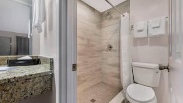Une salle de bain moderne dotée d’un comptoir en granit, d’une douche avec une porte en verre et de toilettes avec un porte-rouleau de papier toilette.