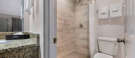 Une salle de bain moderne dotée d’un comptoir en granit, d’une douche avec une porte en verre et de toilettes avec un porte-rouleau de papier toilette.