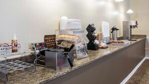 A breakfast bar with a coffee machine, muffin tray, and a sign indicating the breakfast menu. - Rodeway Inn Lyons - La Grange (Lyons)
