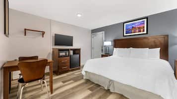 A hotel room with a bed, a desk with a chair, a television, a small refrigerator, and a picture on the wall.