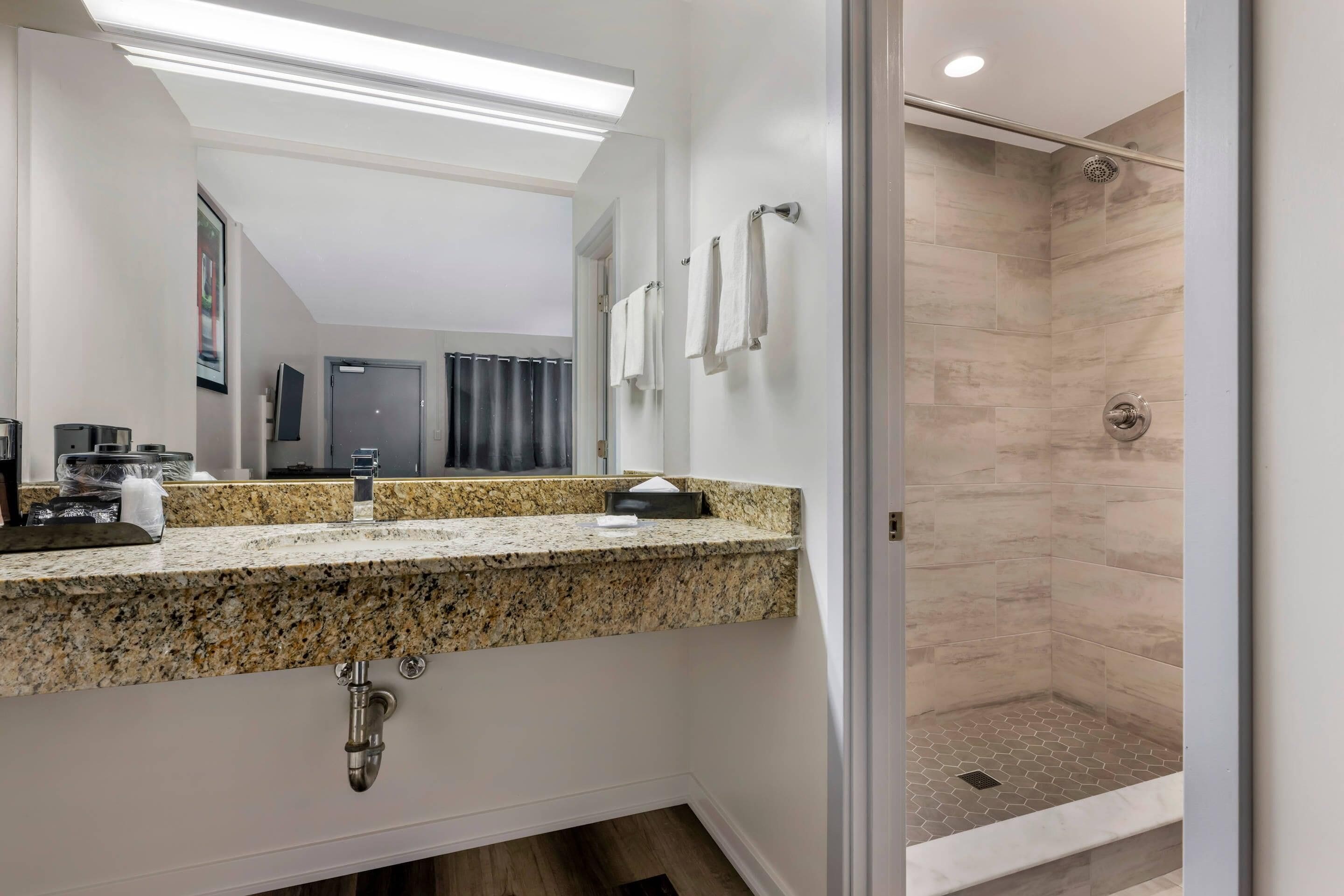 A modern bathroom with a granite countertop, a sink, and a shower area.