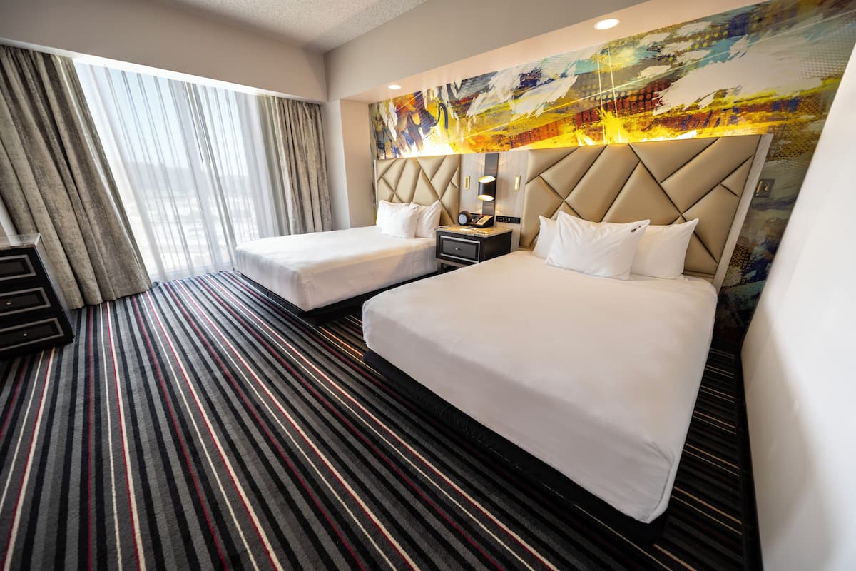 Habitación de hotel con dos camas, alfombra a rayas, un cuadro abstracto grande en la pared y una ventana con cortinas.