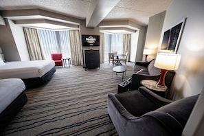 Habitación de hotel con cama, sofá, escritorio, televisión y zona de comedor.