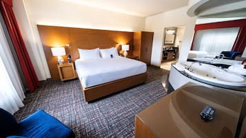 A hotel room with a large bed, bedside lamps, a desk with a chair, a bathroom with a sink and bathtub, and a mirror.