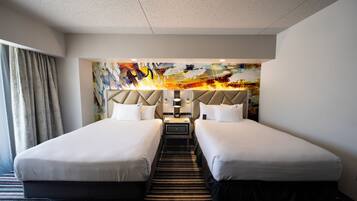 Une chambre d’hôtel avec deux lits, une moquette à rayures, une tête de lit moderne et un tableau abstrait aux couleurs vives accroché au mur.