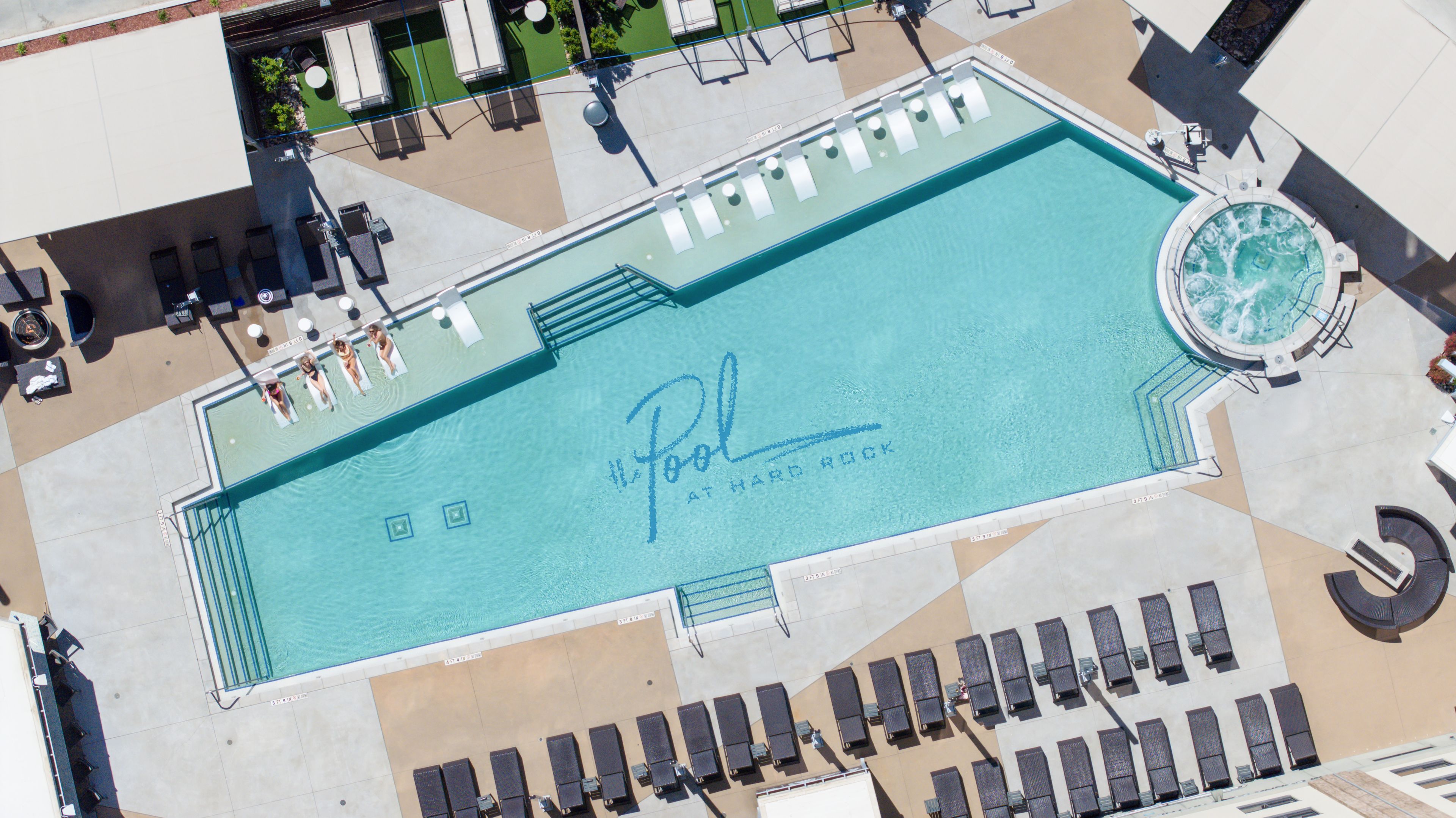 An aerial view of a swimming pool with lounge chairs and a hot tub.