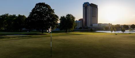 Un campo de golf con una bandera, árboles y un edificio al fondo.