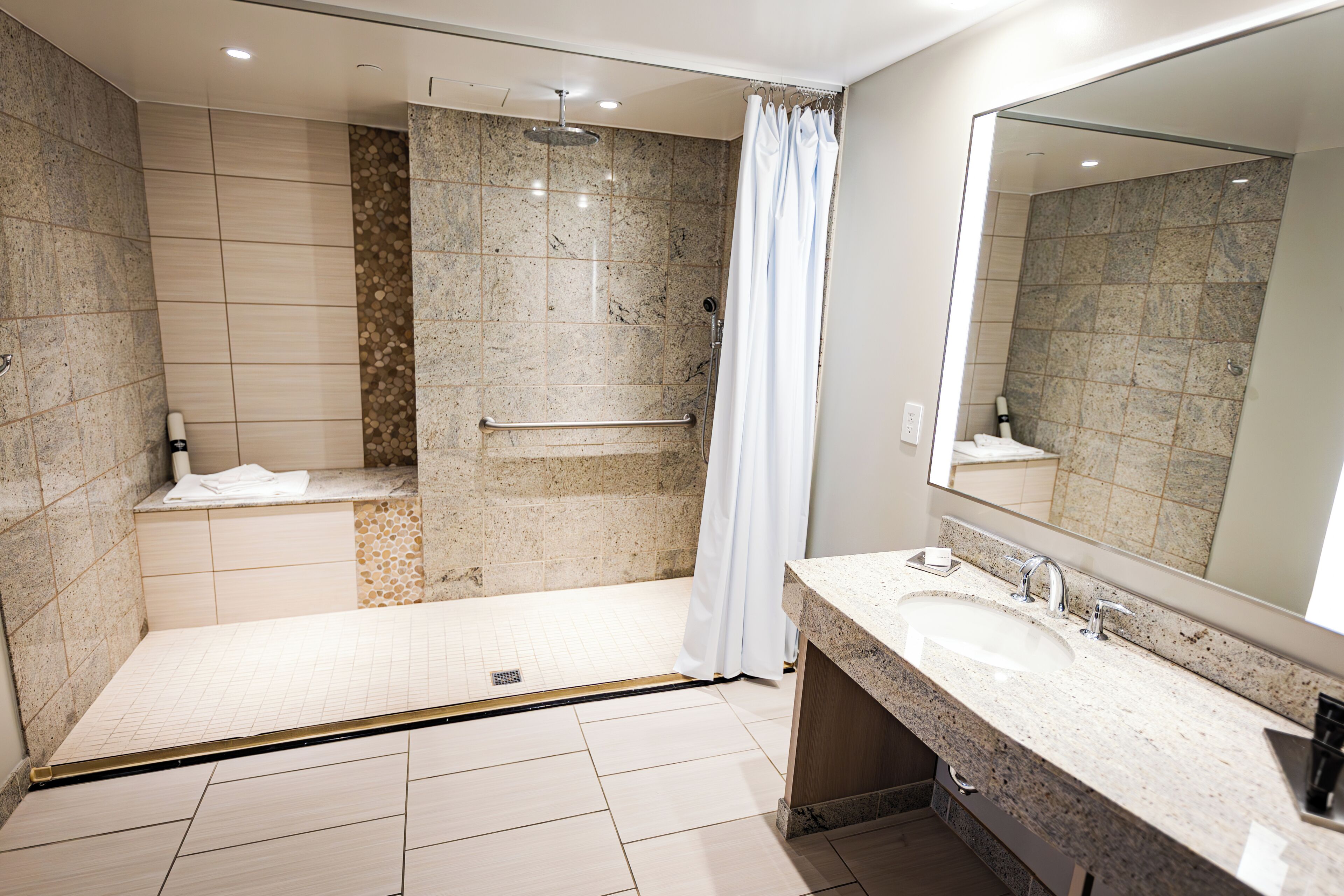 Un bagno moderno con doccia a pavimento, un mobile lavabo e uno specchio grande.
