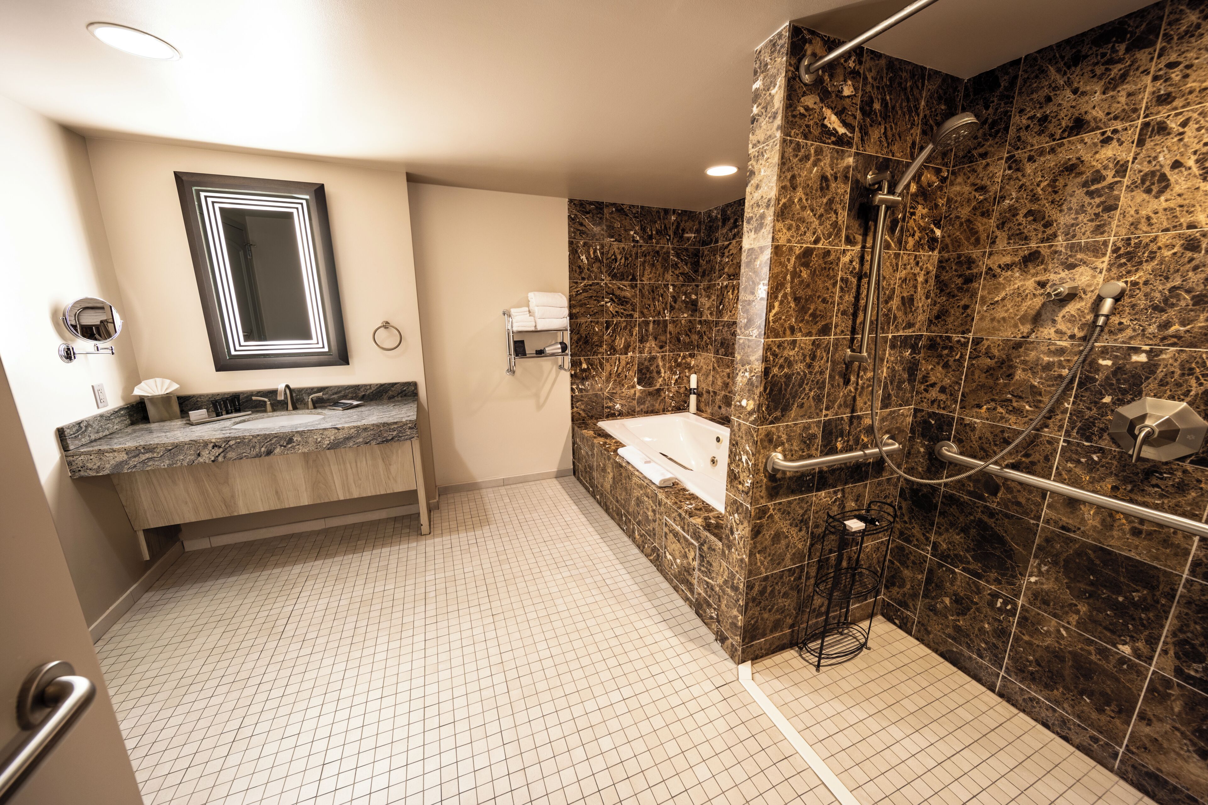 Un baño moderno con ducha de mármol, lavabo integrado y un espejo grande.