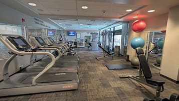 Un gimnasio con cintas de correr, máquinas de pesas y pelotas de ejercicio.