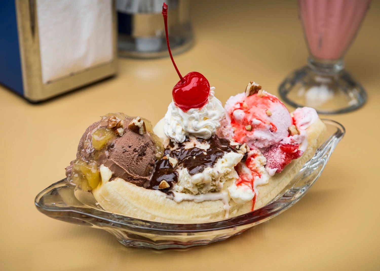 A dessert with multiple scoops of ice cream and toppings on a glass plate.