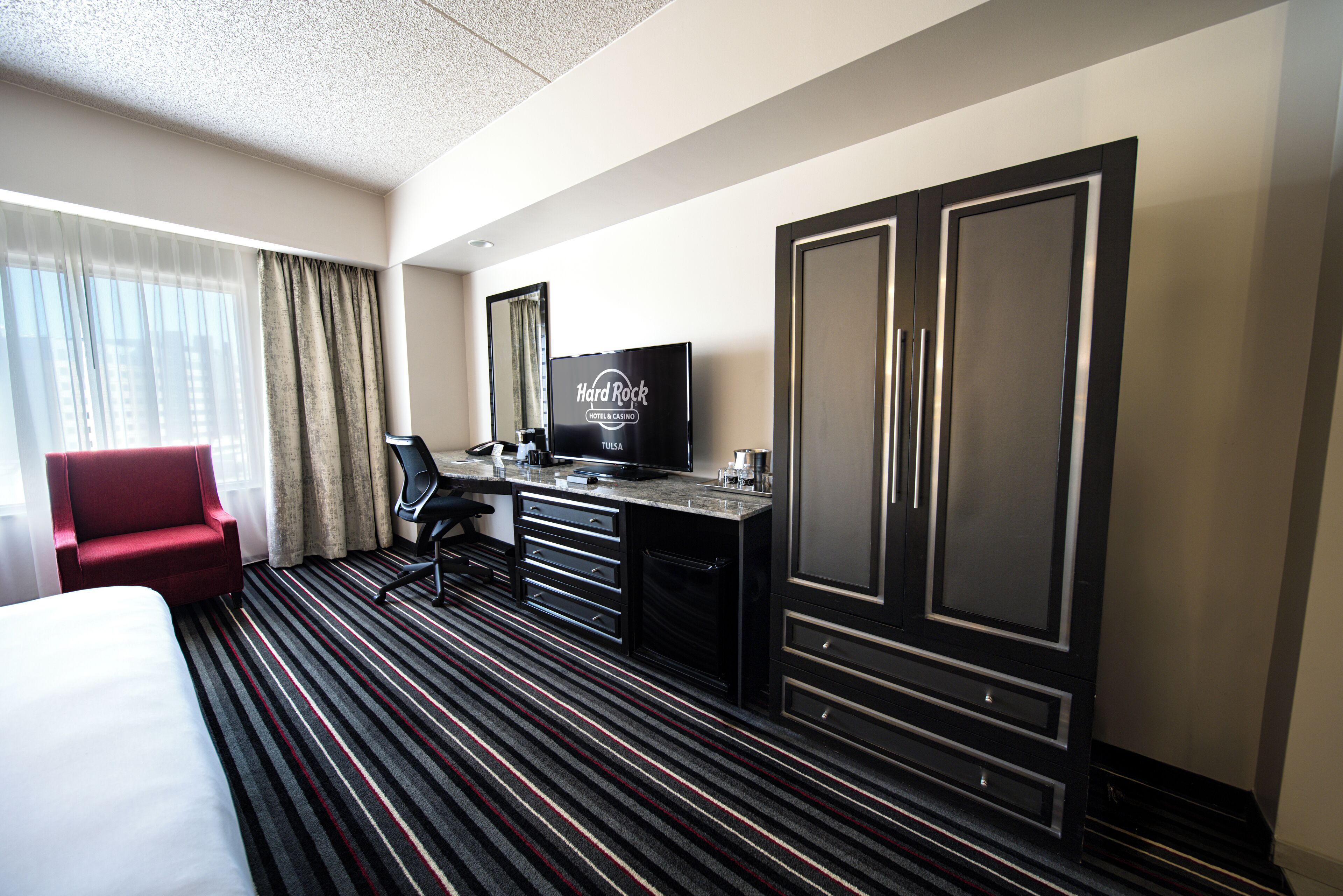 Una habitación de hotel con cama, escritorio, silla, televisor y armario.