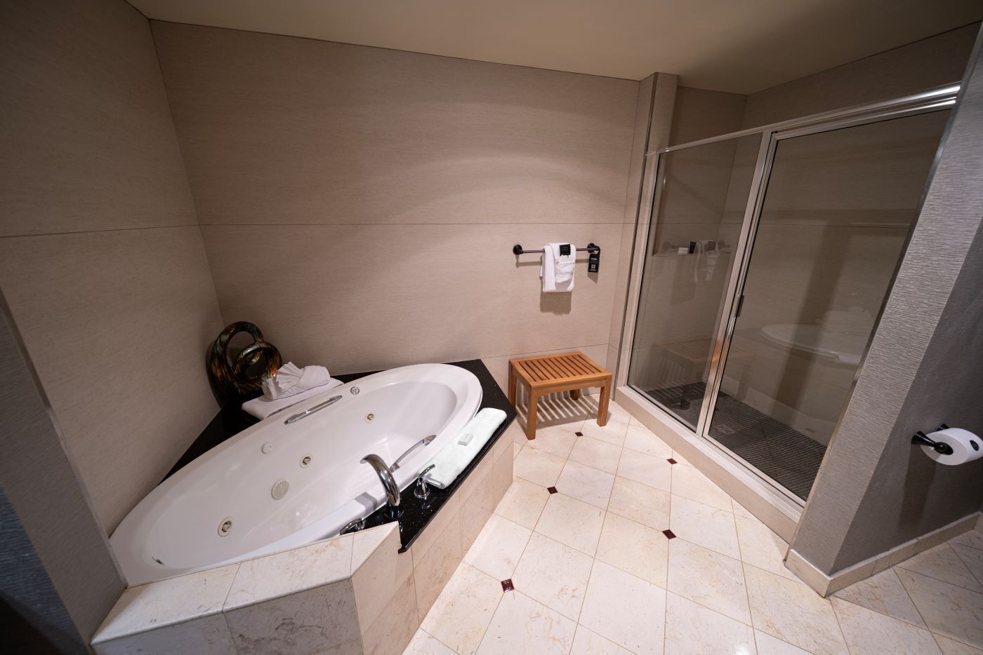 A modern bathroom with a large bathtub, a glass shower enclosure, and a small wooden stool.