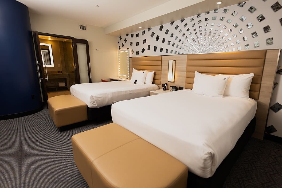 Habitación de hotel con dos camas, una zona de estar y un espejo con luces.
