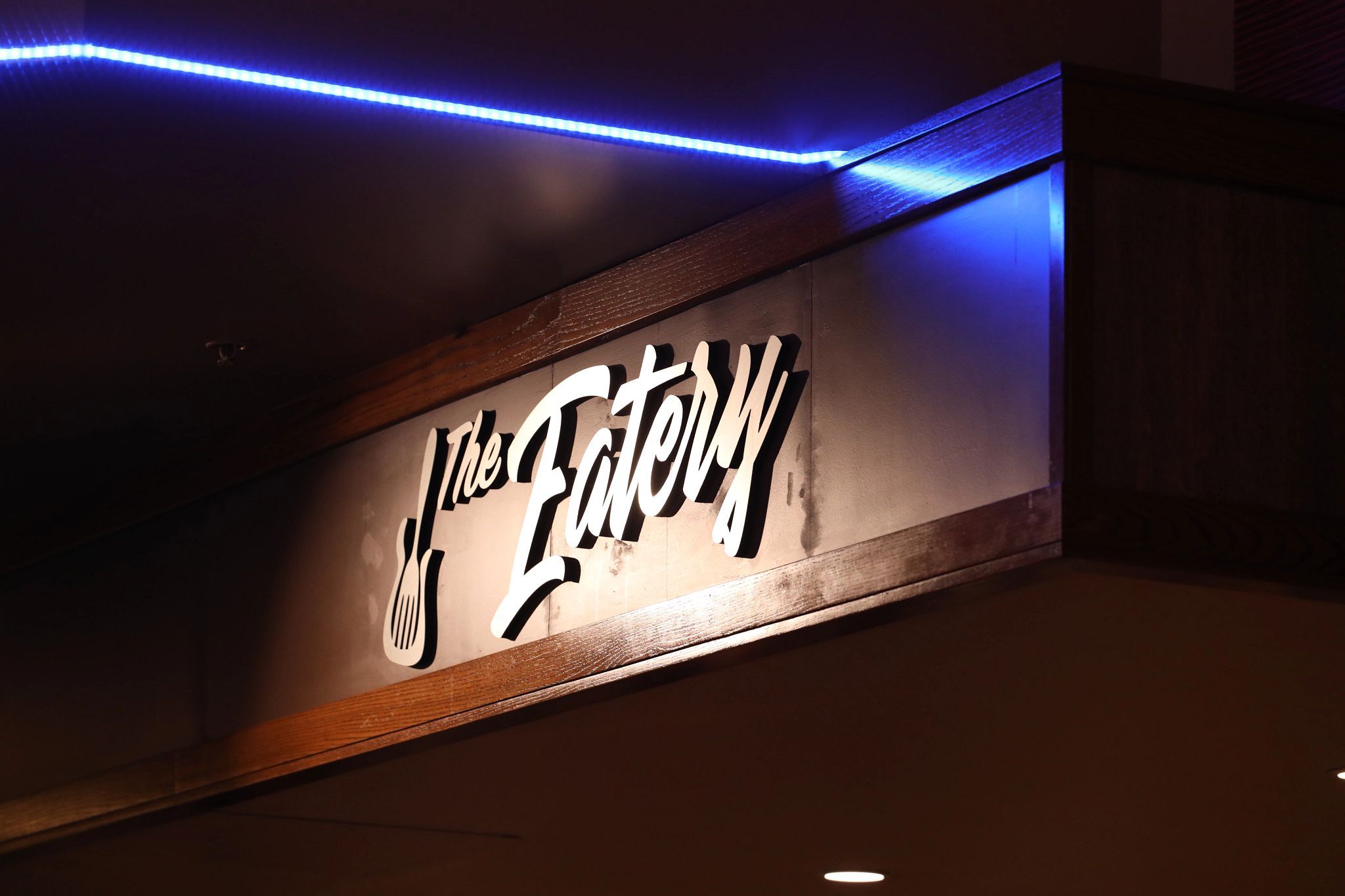 Ein Schild mit der Aufschrift 'The Eatery', beleuchtet durch blaue LED-Leuchten.