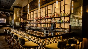 A bar area with a long counter, multiple stools, and shelves stocked with bottles. - Hard Rock Hotel and Casino Tulsa (Catoosa)