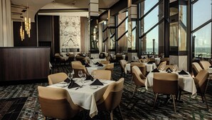 A modern restaurant with high ceilings, large windows, and a marble wall. Tables are set with white tablecloths and brown chairs. - Hard Rock Hotel and Casino Tulsa (Catoosa)