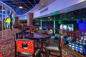 Zona de casino con mesas de juego, sillas y máquinas tragamonedas.