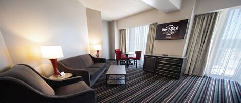 A hotel room with a sofa, a coffee table, a TV, and a dining area with chairs.