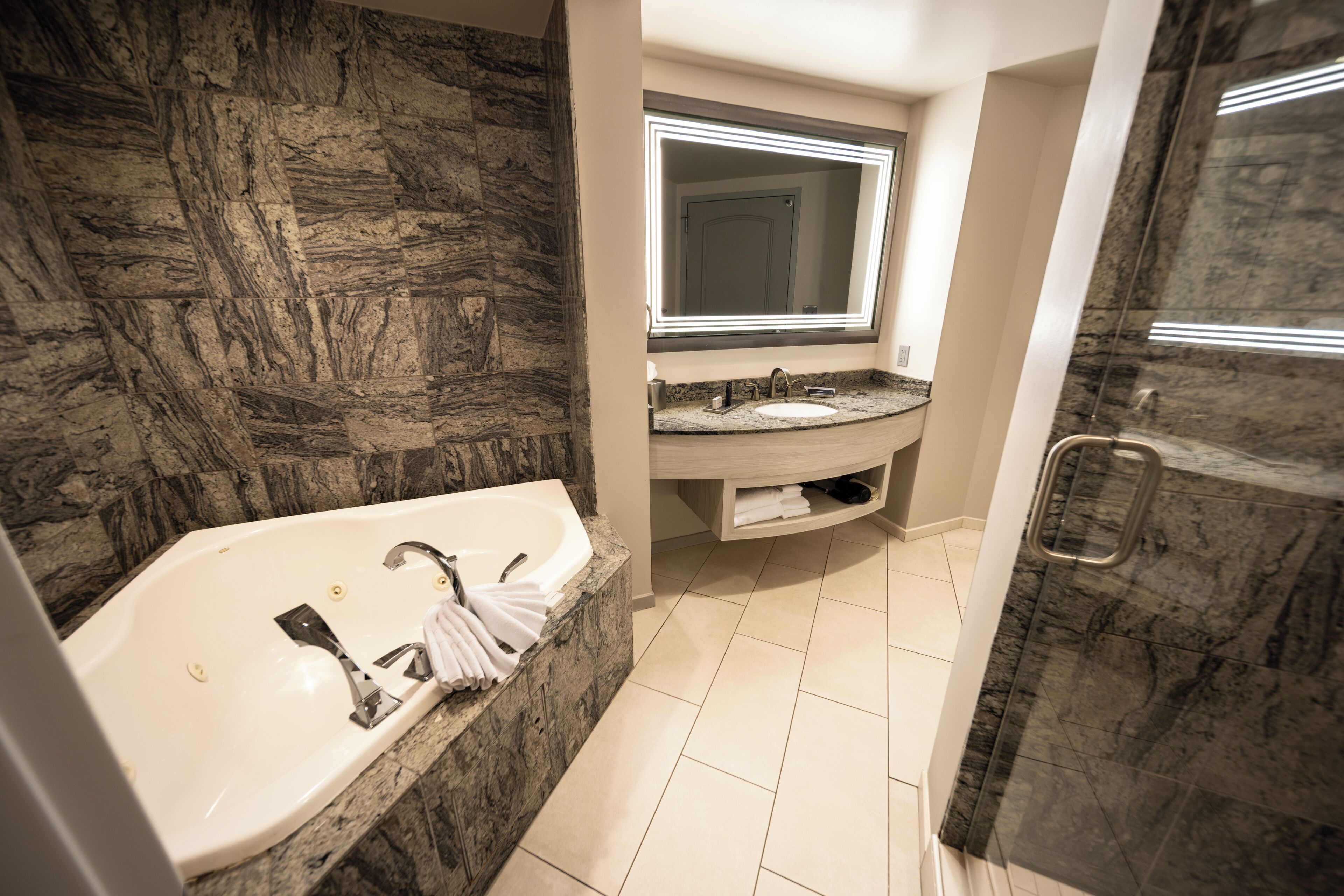 A modern bathroom with a marble sink, a large mirror, and a separate shower area.