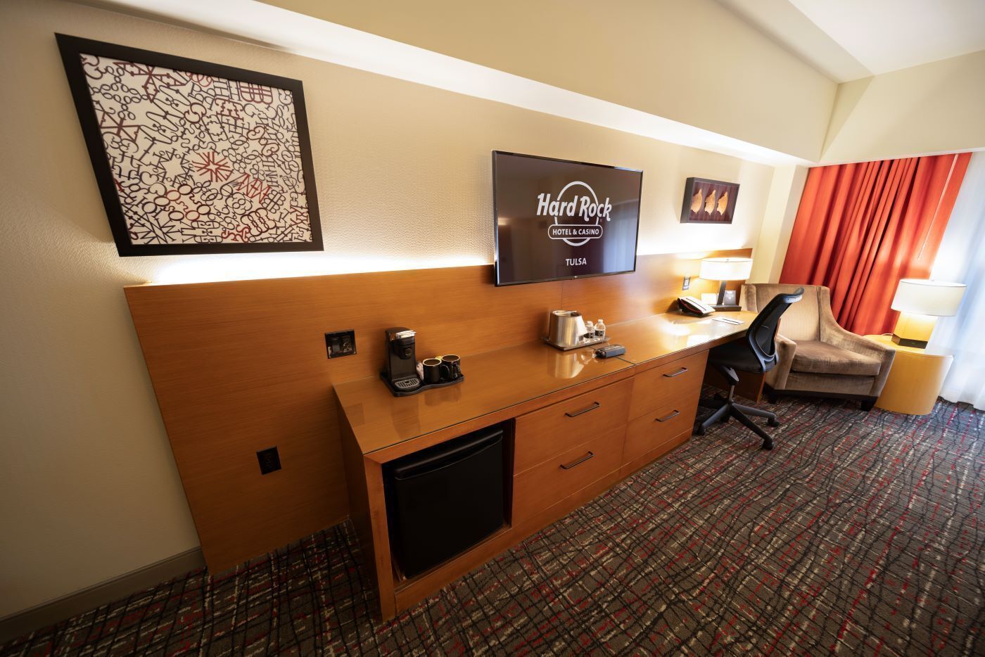 A hotel room with a wooden desk, a coffee maker, a TV, and a chair.