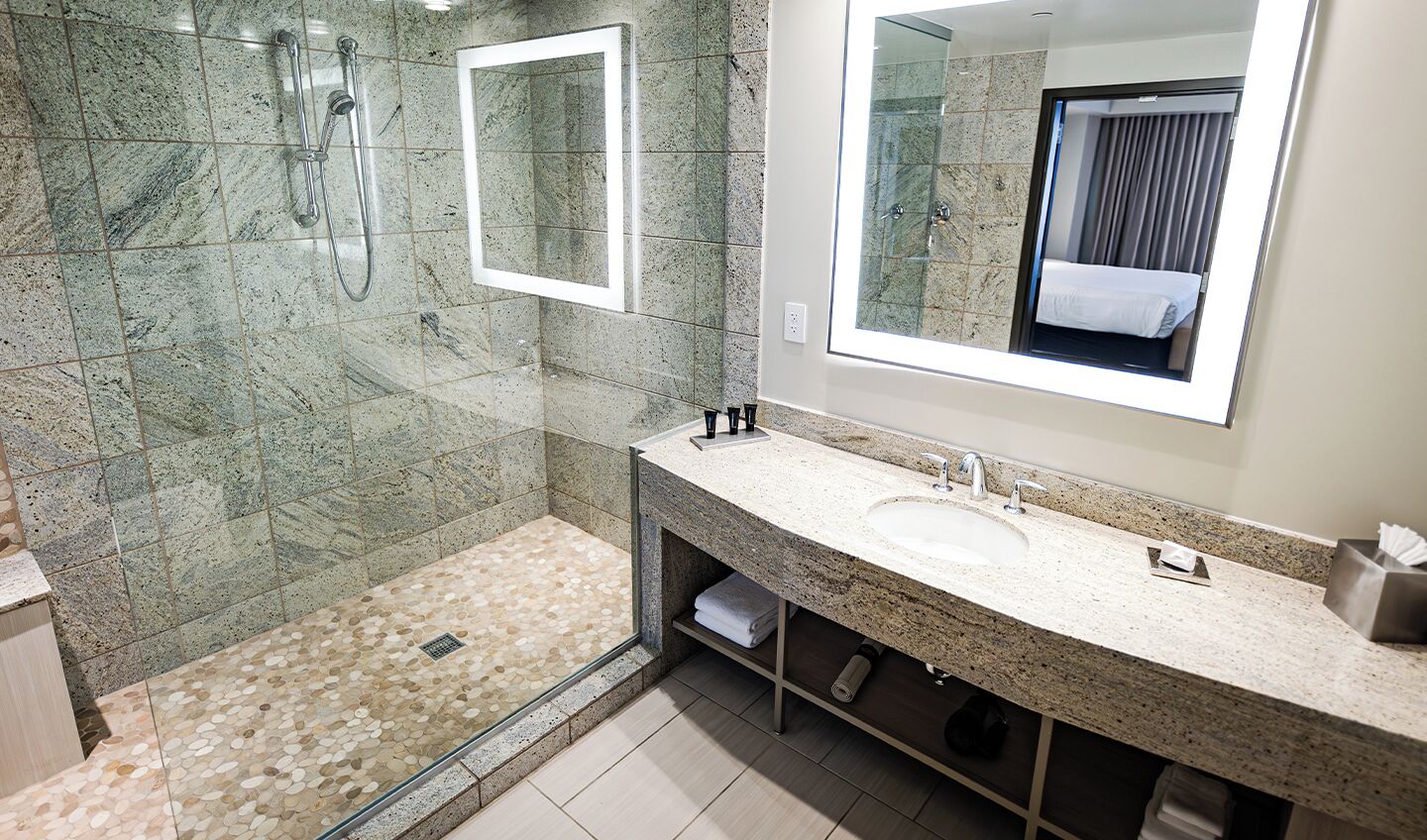Un baño moderno con encimera de granito, ducha con mampara de vidrio y un espejo grande.