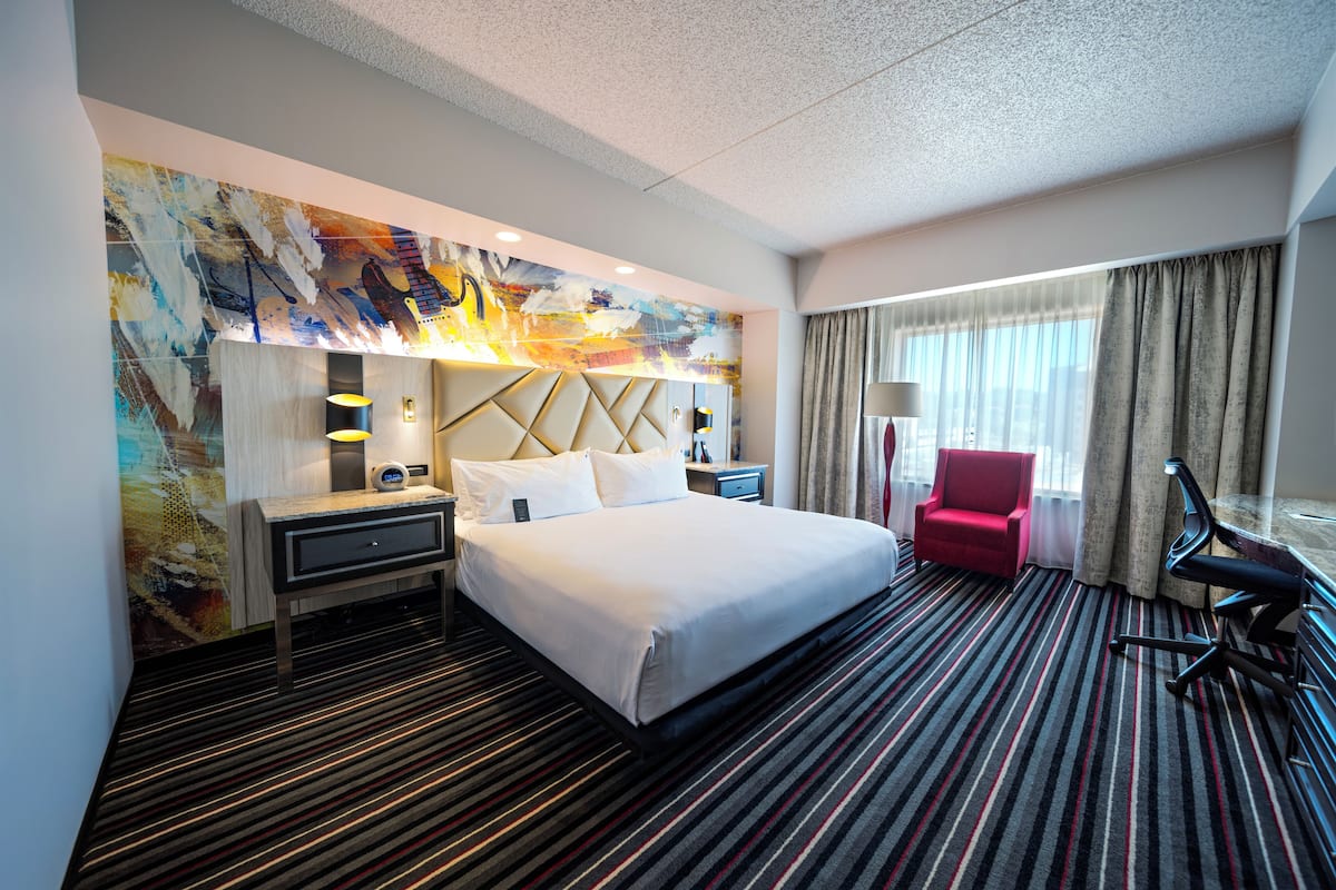Habitación de hotel con una cama grande, un escritorio, una silla, una lámpara de escritorio y un cuadro abstracto de colores en la pared.