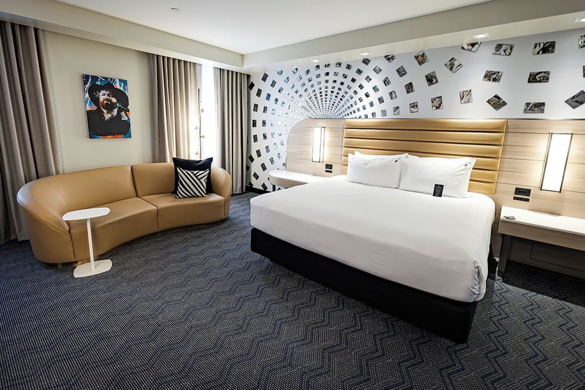 Una habitación de hotel moderna con una cama grande, un sofá curvo, una mesita auxiliar y una pared decorada con fotografías.