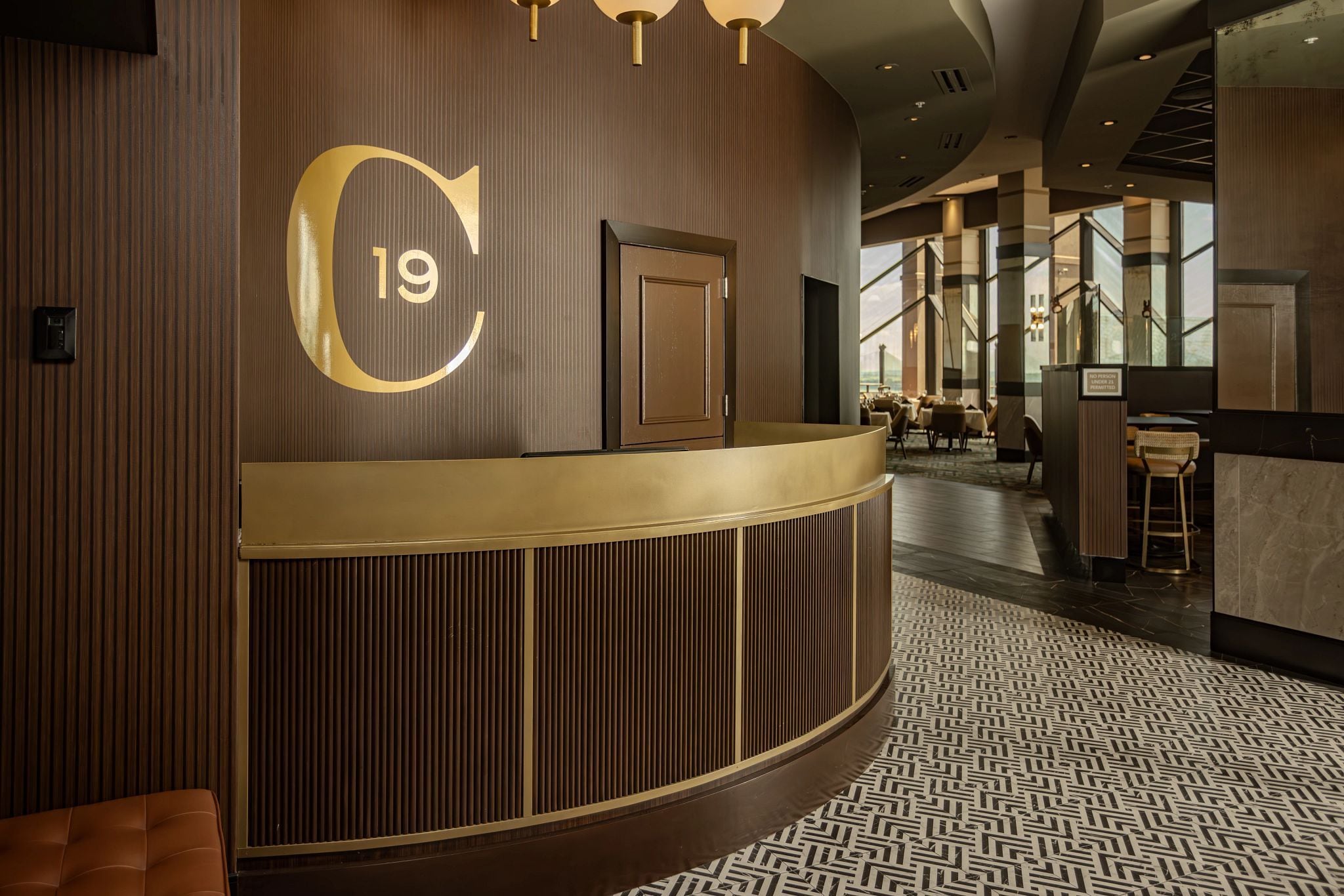 Zona de recepción de hotel con un gran letrero con el número 19, un mostrador de recepción y un suelo estampado.