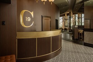 Zona de recepción de hotel con un gran letrero con el número 19, un mostrador de recepción y un suelo estampado.