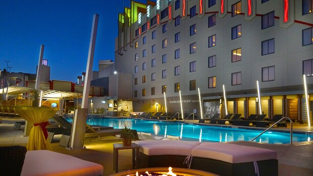 A hotel pool area with lounge chairs, a fire pit, and a large building in the background. - Hard Rock Hotel and Casino Tulsa (Catoosa)
