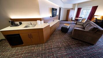 Habitación de hotel con kitchenette, sofá, televisión y alfombra estampada.