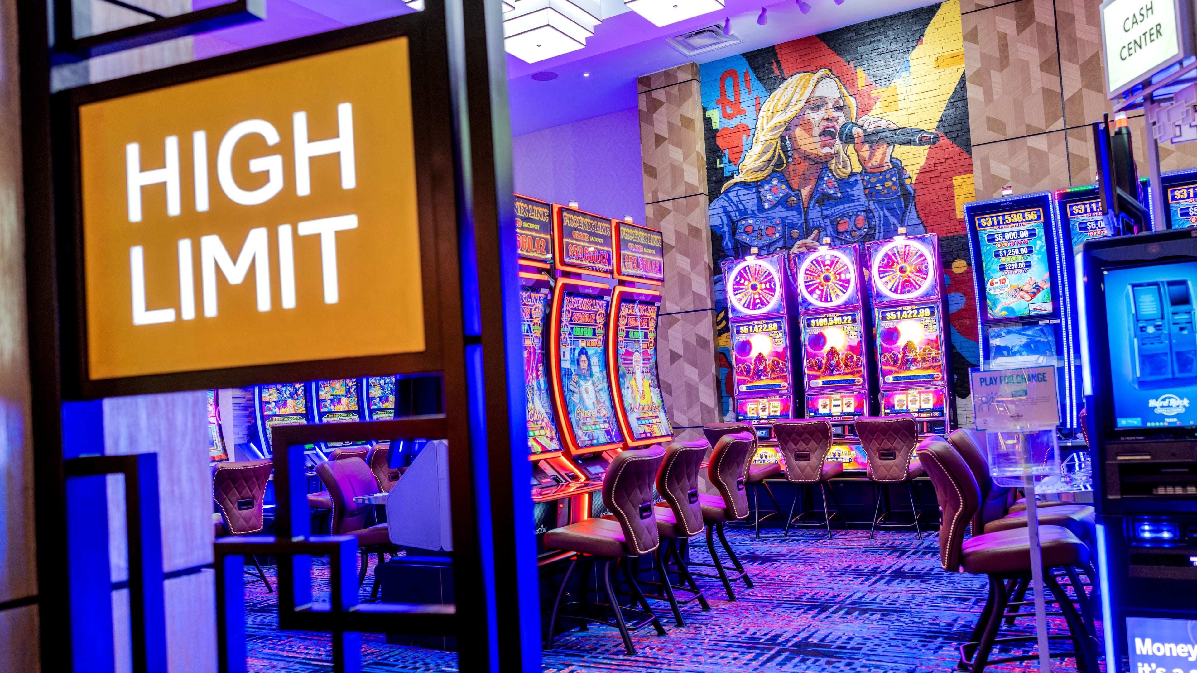 Zona de casino con máquinas tragamonedas, un letrero que dice 'HIGH LIMIT' y un mural en la pared.